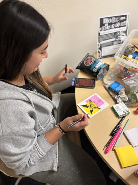 Photo shows a woman working on a small zine.