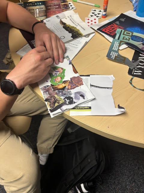 Photo shows the hands of a zinester as they work on putting material into a zine at a project table.